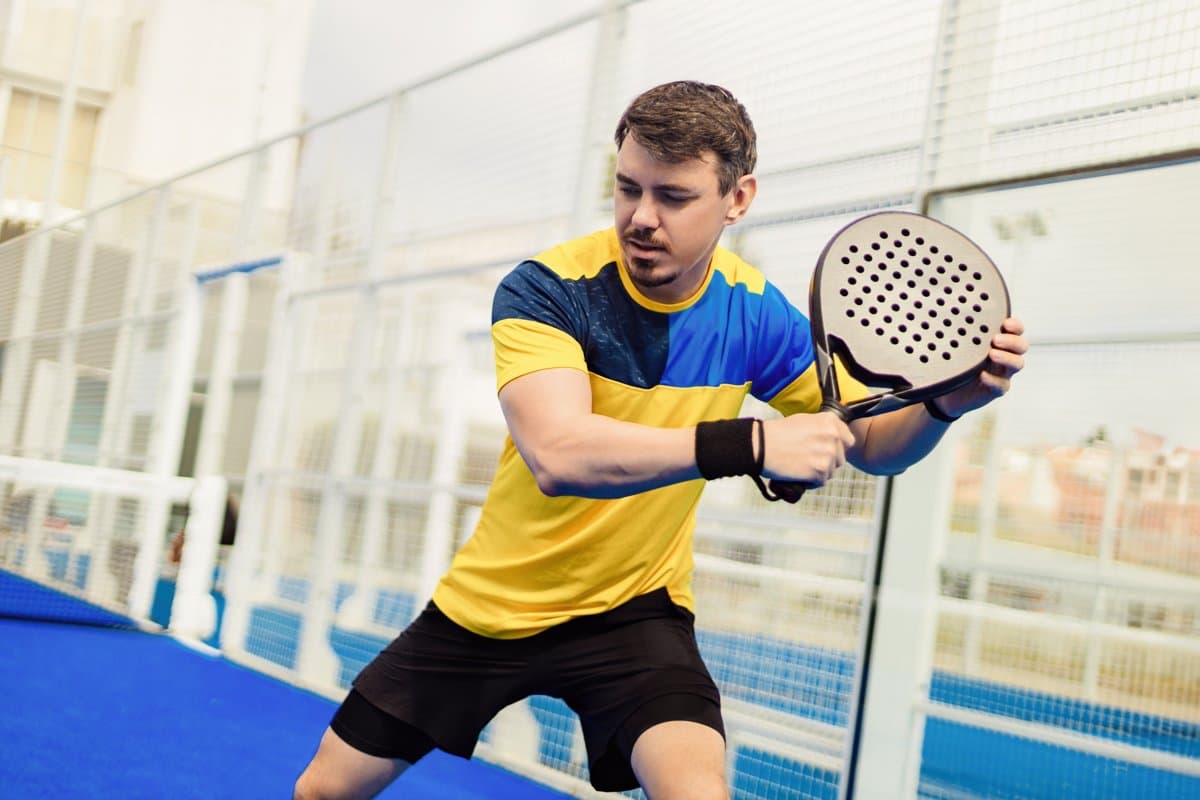Aksi pemain padel pria bersiap melakukan pukulan di lapangan biru